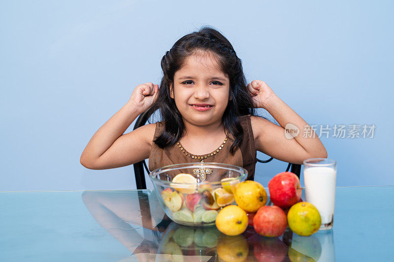 Cute Asian/ Indian little child girl making strong hand while drinking a milk for breakfast.